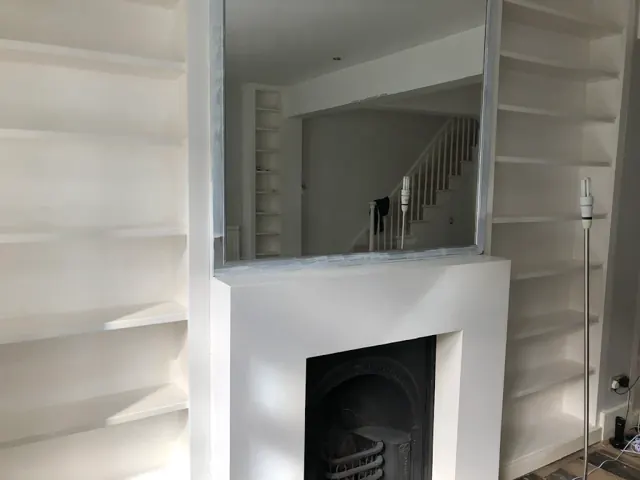 Large mirror hung above a painted fireplace between alcove shelves